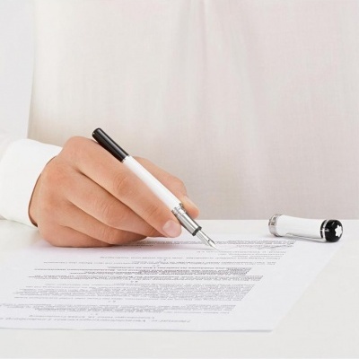 Mão escrevendo num documento com caneta preta e branca