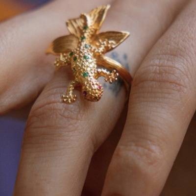 Anel dourado em forma de lagarto com pedras coloridas na mão