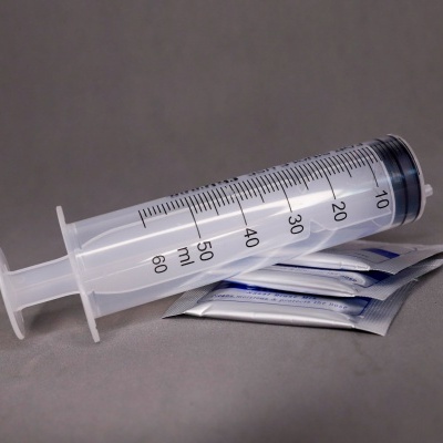 Seringa plástica de 60 ml com escala em preto encostada em sachês embalados