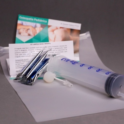 kit com seringa plástica, tubos metálicos, ampola, folhetos e material sobre superfície cinza