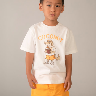 Criança com camisola branca com estampa de jacaré e texto COCONUT e calções laranja