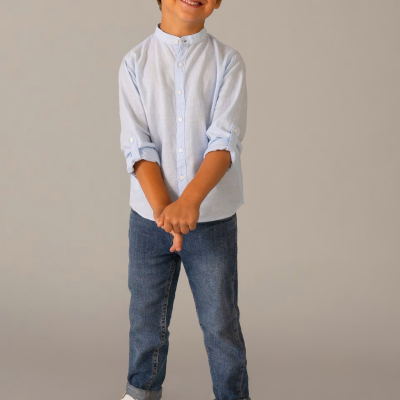 Menino com camisa azul clara, calças de ganga e ténis brancos