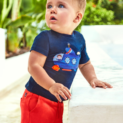 Criança com roupa de verão com estampado de submarino, ao ar livre junto a uma parede branca