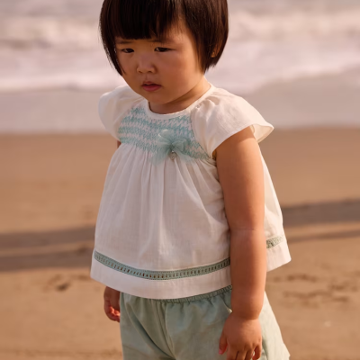 Criança com roupa de verão branca e azul claro em praia