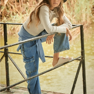 Menina com chapéu azul escuro e roupa casual junto a água numa estrutura metálica