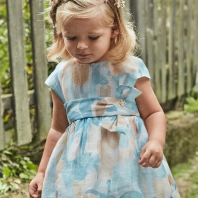 Menina com vestido azul, bege e branco e coroa de flores em ambiente exterior