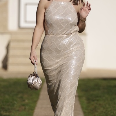 Mulher com vestido pérola brilhante e mala pequena de cetim num passeio ao ar livre