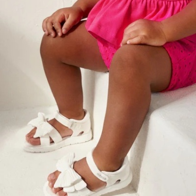 Criança sentada com roupa cor-de-rosa e sandálias brancas com laços