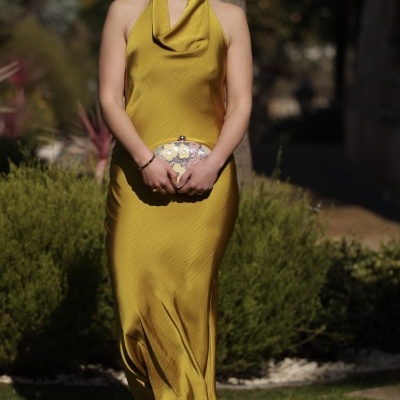 Mulher com vestido amarelo longo e mala de mão floral ao ar livre