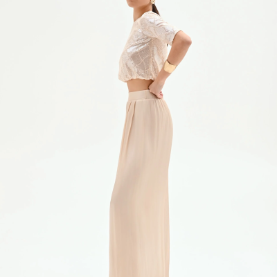Mulher de perfil com blusa cropped brilhante bege e saia longa bege clara