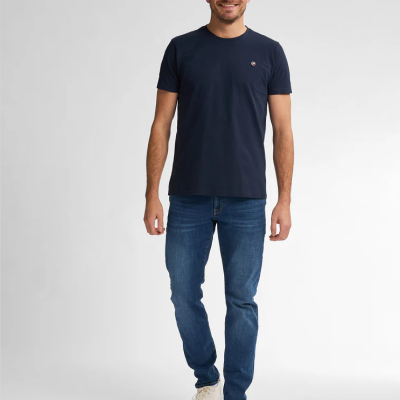 Homem vestido com camiseta azul escura, calças de ganga e sapatilhas brancas
