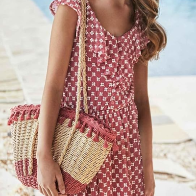 Criança com vestido rosa de flores pequenas brancas e mala de palha rosa junto a piscina
