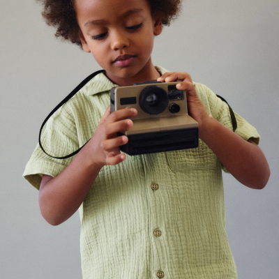 Criança com roupa verde claro a segurar uma câmara fotográfica instantânea bege e preta