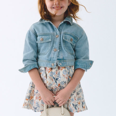 Criança com casaco de ganga azul e vestido floral a segurara mala creme.