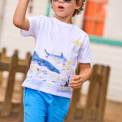Camiseta branca de criança com estampa de tubarões e calções azuis