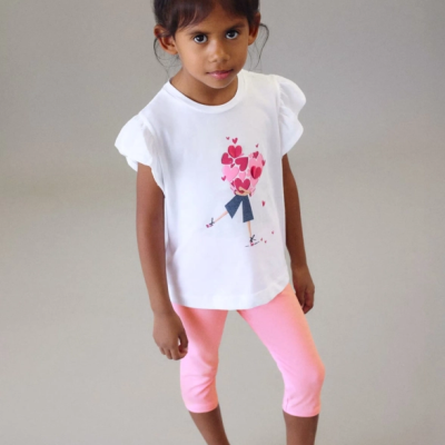 Criança vestida com t-shirt branca estampada e calças rosas 3/4 com sandálias brancas