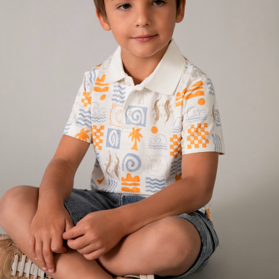 Camisola polo branca com padrões laranja, azul e castanho, calções de ganga cinza e sapatilhas bege para criança