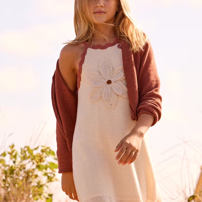 Criança com vestido de malha creme e cardigan rosa escuro ao ar livre