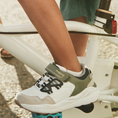 Ténis infantis branco, cinza e verde com velcro mayoral numa bicicleta branca.