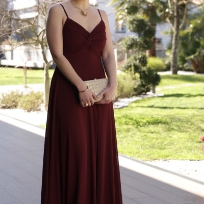 Mulher com vestido longo vinho segurando mala prateada ao ar livre