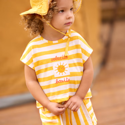 Criança com chapéu amarelo e roupa às riscas amarelas e brancas com sol sorridente