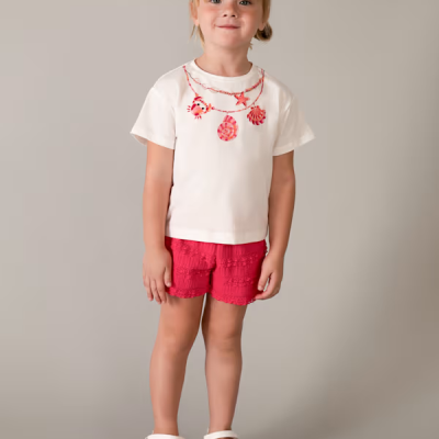 Camisola branca com estampado vermelho, calções vermelhos texturizados e sandálias brancas em fundo cinza.