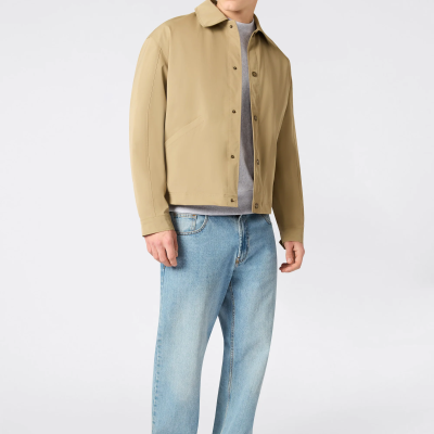 Homem com casaco bege, t-shirt cinza, calças de ganga azuis e sapatilhas brancas, fundo branco