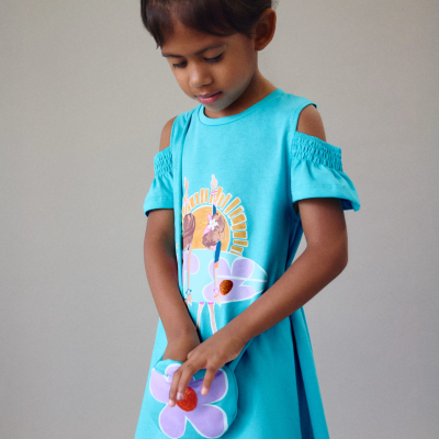 Criança de vestido azul turquesa com estampa colorida e bolsinha em formato de flor
