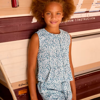Criança de cabelo afro com roupa azul e branca junto a caravana marrom e bege
