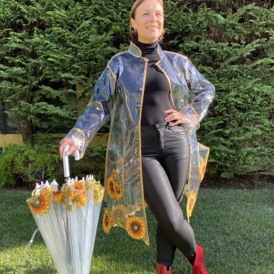 Mulher de casaco transparente com girassóis a segurar guarda-chuva com girassóis em relvado