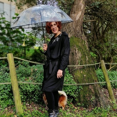 Mulher com vestido preto e guarda-chuva prateado com padrões, em ambiente natural