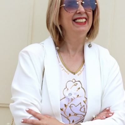 Mulher com óculos de sol redondos e casaco branco a sorrir