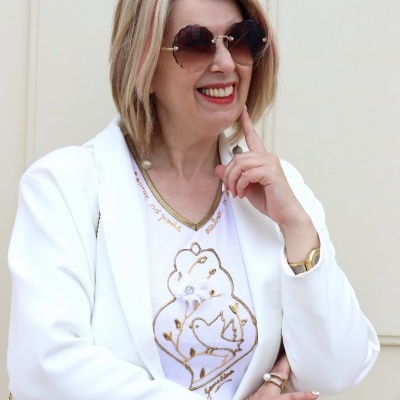 Mulher de cabelo loiro curto com óculos de sol e casaco branco em fundo claro