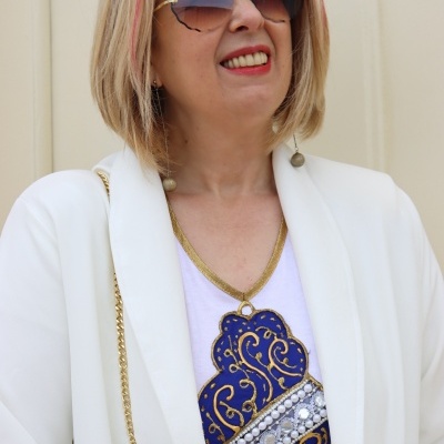 Mulher com óculos de sol, camisa branca com padrão azul e casaco branco