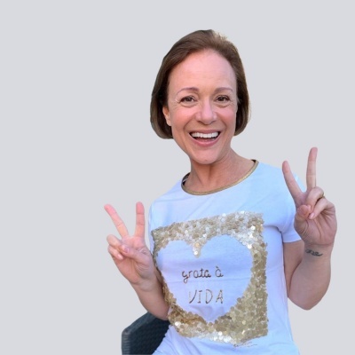 Mulher sorridente com camiseta branca com coração dourado de lantejoulas e texto 
