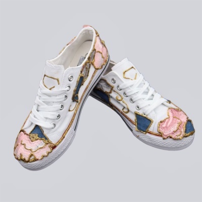 Sapatilhas brancas com bordados coloridos e atacadores brancos sobre fundo cinza