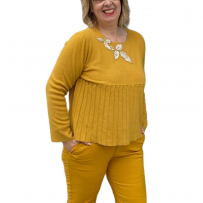 Mulher com conjunto amarelo mostarda, camisola com bordado de folhas e calças lisas