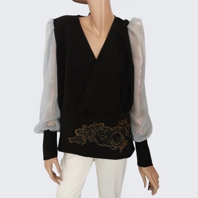 Blusa preta com mangas brancas transparentes e detalhe dourado, combinada com calças brancas