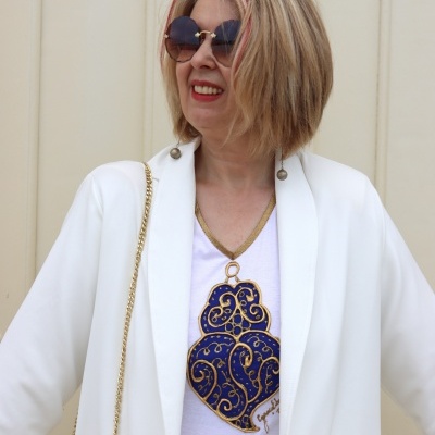Mulher com blazer branco, óculos de sol e camisola branca com estampado azul e dourado