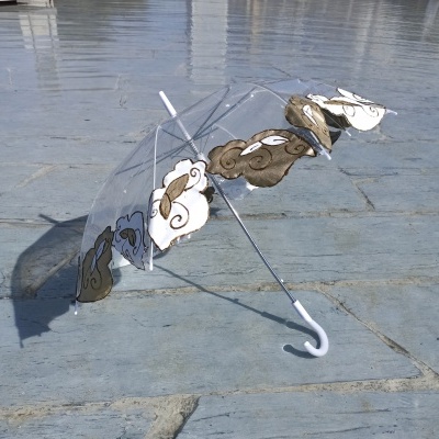 Guarda-chuva transparente com nuvens coloridas pousado no chão de pedra