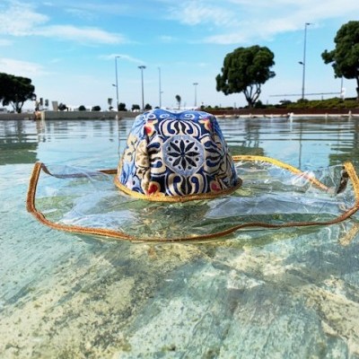 Chapéu colorido com viseira transparente sobre água, com céu e árvores ao fundo