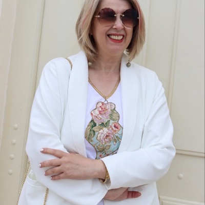 Mulher com casaco branco e t-shirt branca com padrão floral, óculos de sol castanhos