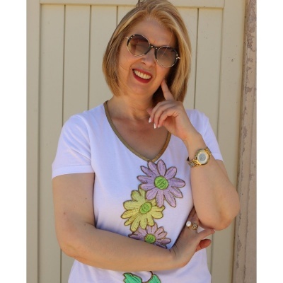 Mulher loira com óculos de sol, camisa branca com flores bordadas e relógio dourado