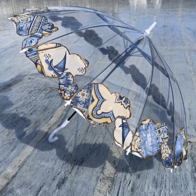 Guarda-chuva transparente com padrão azul e bege na borda sobre chão de cimento cinzento