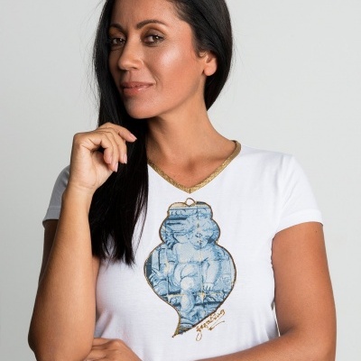 Mulher com t-shirt branca com estampa de anjo azul e gola dourada num fundo cinza claro