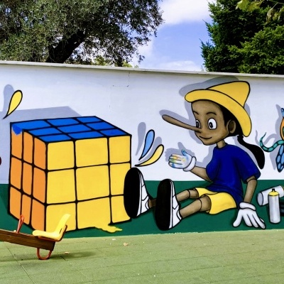 Mural com cubo mágico, personagem sentado com chapéu amarelo e escorrega de madeira