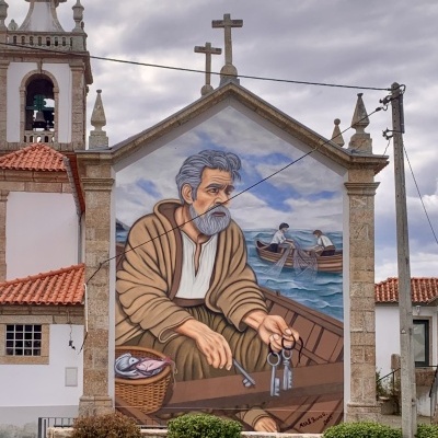 Mural de um homem idoso num barco a segurar chaves e um cesto com peixes diante de dois homens num barco no mar.