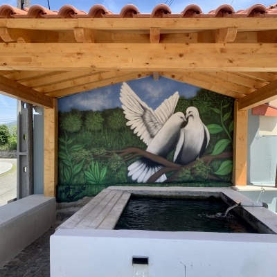 Tanque de pedra branco com água sob estrutura de madeira e pintura mural de pombos brancos
