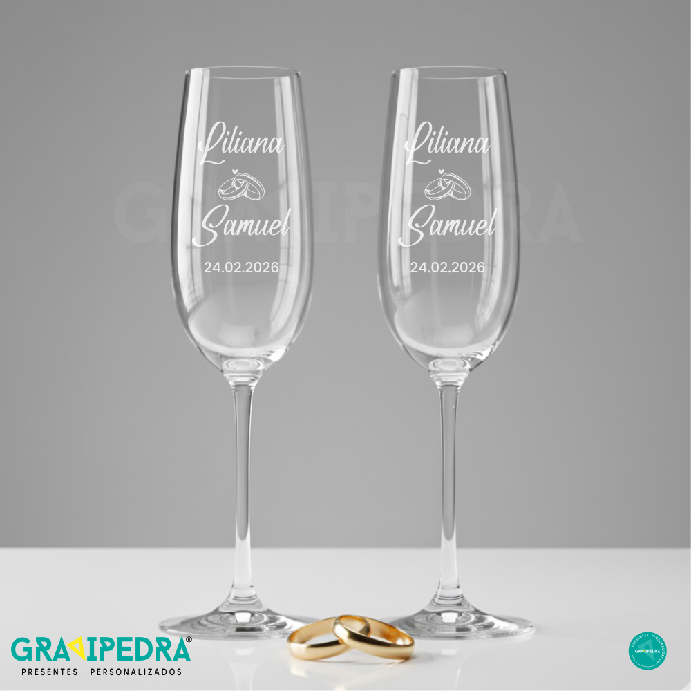 Pack 2 Copos em vidro personalizados - Casamento - CVCND22A Dois copos de champanhe personalizados com nomes e data, e duas alianças douradas em frente.