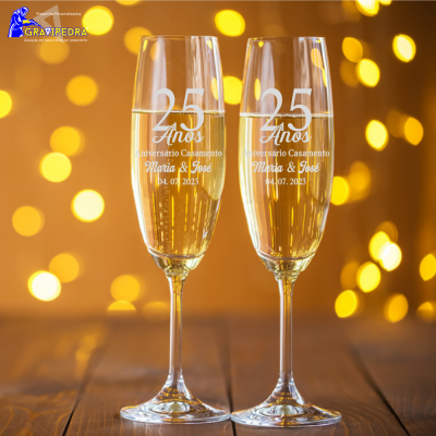 Dois copos de champanhe gravados para aniversário de casamento sobre mesa de madeira com luzes amarelas ao fundo